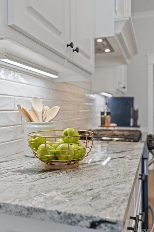 room details with decorative backsplash, light stone countertops, and white cabinets