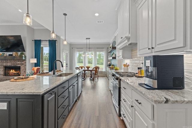 kitchen featuring pendant lighting, white cabinetry, a brick fireplace, stainless steel appliances, and a center island with sink