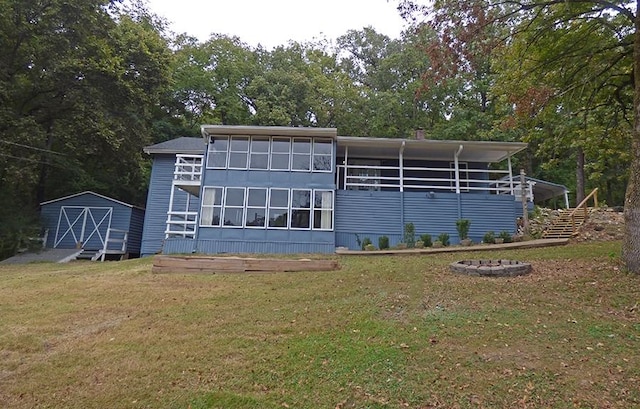 back of house with a storage shed, a lawn, and a fire pit