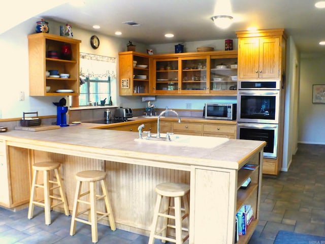 kitchen with appliances with stainless steel finishes, a kitchen breakfast bar, kitchen peninsula, tile countertops, and sink