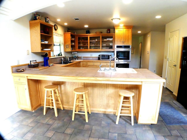 kitchen featuring tile counters, kitchen peninsula, appliances with stainless steel finishes, and a breakfast bar area