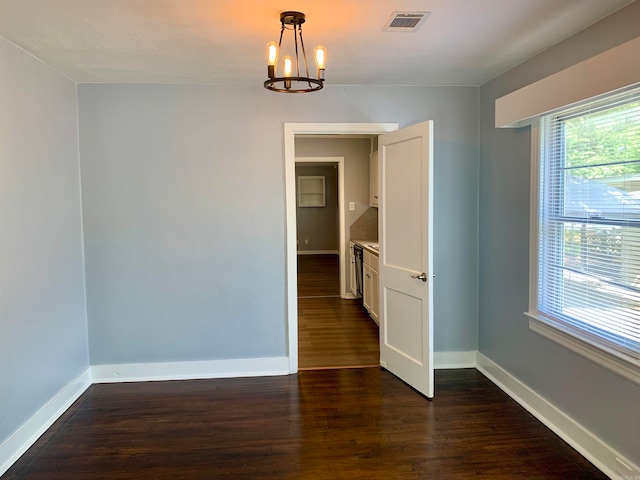 spare room with an inviting chandelier and dark hardwood / wood-style floors