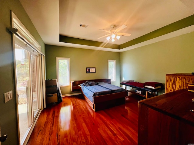 bedroom with ceiling fan, a raised ceiling, hardwood / wood-style floors, and access to outside