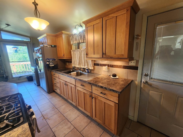 kitchen featuring hanging light fixtures, decorative backsplash, light tile patterned flooring, stainless steel fridge, and stove