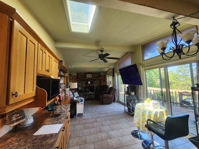 kitchen with ceiling fan with notable chandelier, lofted ceiling with skylight, and dark stone countertops