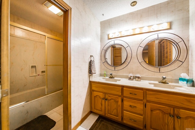 bathroom with a textured ceiling, tile walls, vanity, and shower / bath combination with glass door