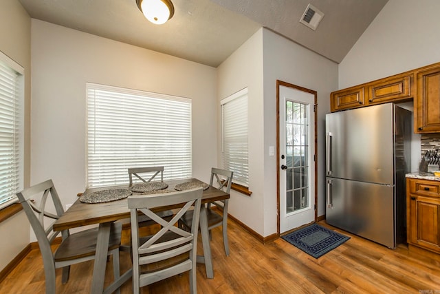 dining area with a textured ceiling, light hardwood / wood-style floors, and vaulted ceiling