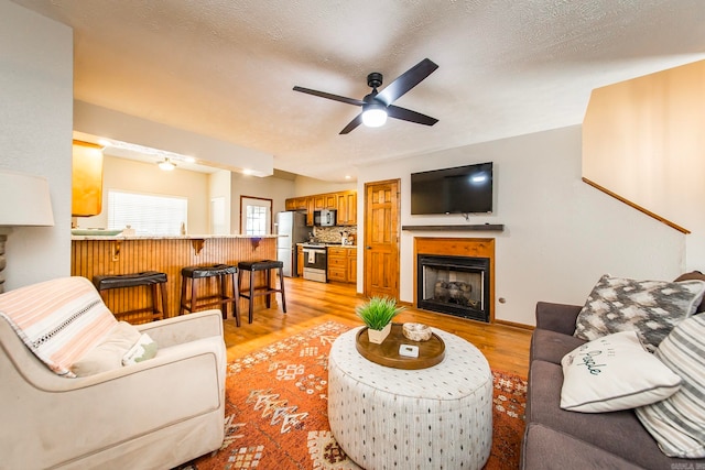 living room with light hardwood / wood-style flooring, ceiling fan, and a textured ceiling