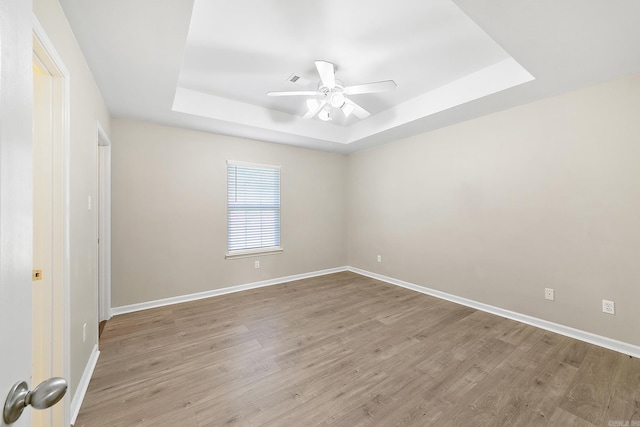 spare room with a tray ceiling, ceiling fan, and light hardwood / wood-style flooring