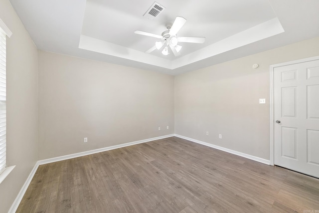 empty room with ceiling fan, a raised ceiling, and wood-type flooring