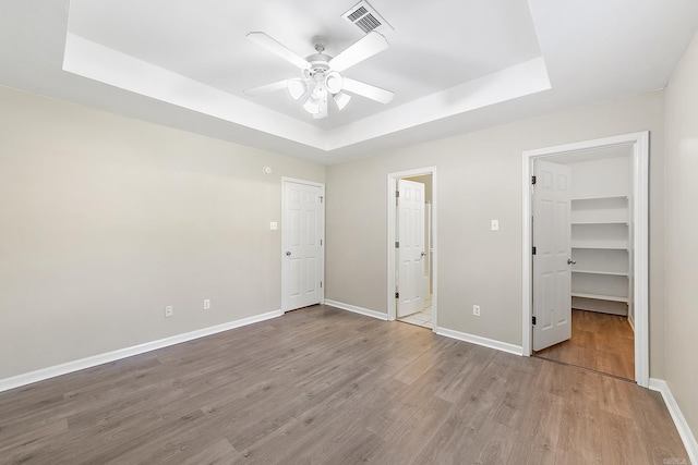 unfurnished bedroom featuring ceiling fan, a closet, a tray ceiling, a spacious closet, and hardwood / wood-style floors