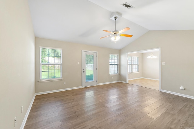 empty room with ceiling fan with notable chandelier, vaulted ceiling, light hardwood / wood-style floors, and plenty of natural light