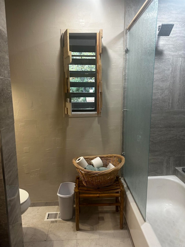 bathroom with toilet and shower / bath combination with glass door