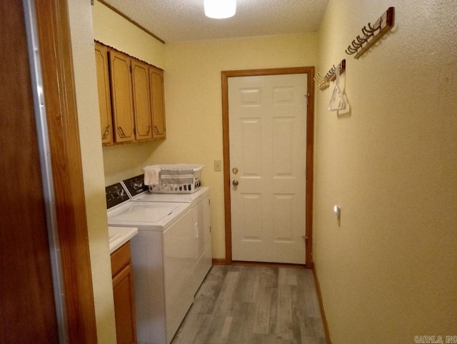 clothes washing area with cabinets, light wood-type flooring, independent washer and dryer, and a textured ceiling