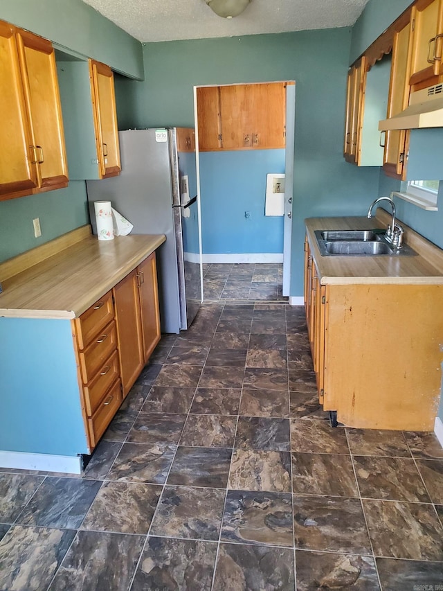 kitchen featuring a textured ceiling, stainless steel fridge, sink, and range hood