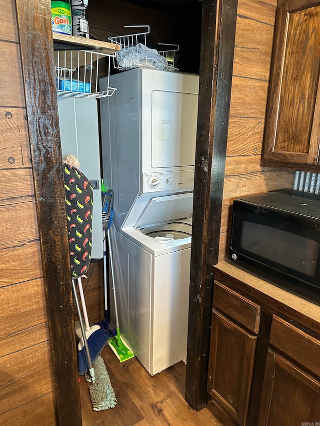 laundry room with wooden walls, dark wood-type flooring, and stacked washer and dryer