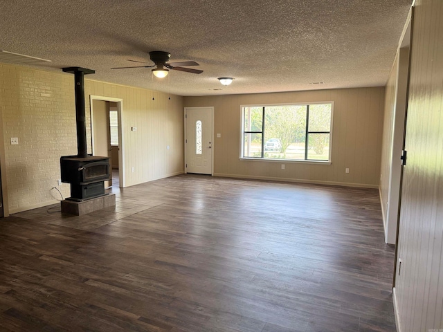 unfurnished living room with ceiling fan, dark hardwood / wood-style floors, a textured ceiling, and a wood stove