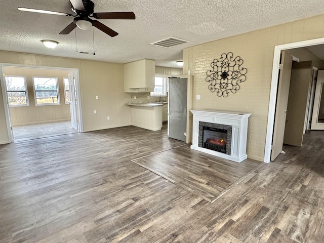 unfurnished living room featuring dark wood-type flooring, sink, a textured ceiling, and ceiling fan