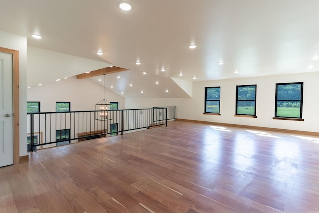 additional living space with an inviting chandelier, lofted ceiling, light wood-type flooring, and a wealth of natural light