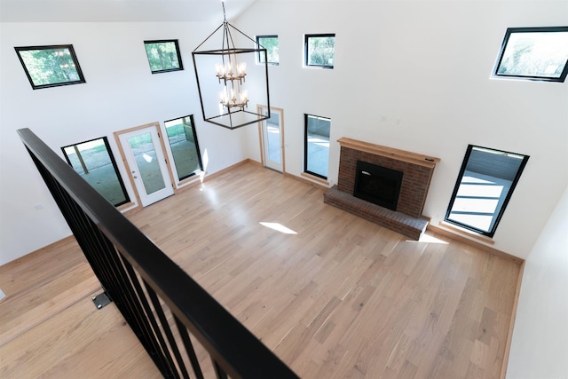 unfurnished living room with a notable chandelier, light hardwood / wood-style floors, a brick fireplace, and high vaulted ceiling