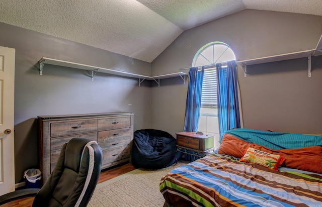 bedroom with vaulted ceiling, a textured ceiling, and hardwood / wood-style flooring