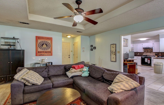 living room featuring ceiling fan, a textured ceiling, light wood-type flooring, and a tray ceiling