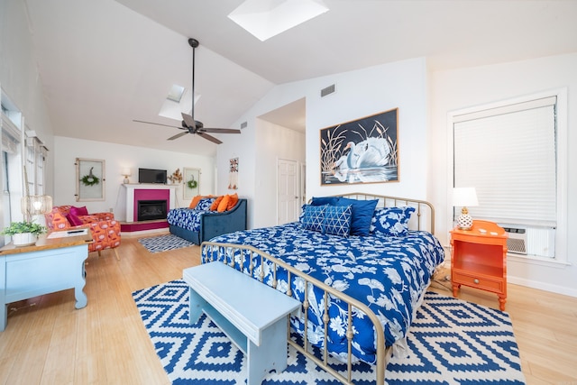 bedroom with ceiling fan, cooling unit, hardwood / wood-style floors, and lofted ceiling with skylight