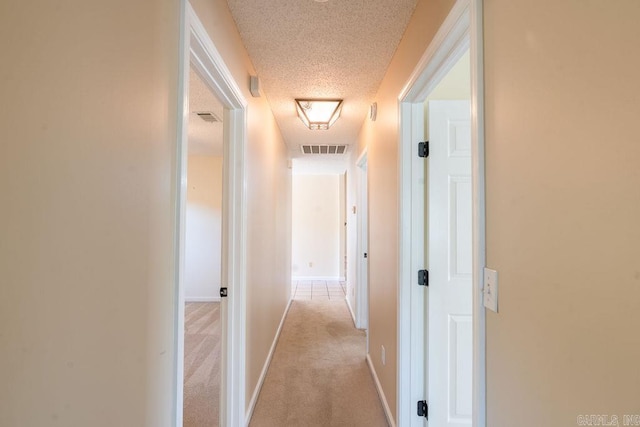 hall featuring light colored carpet and a textured ceiling