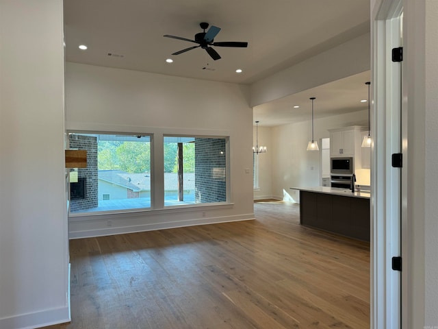 unfurnished living room with light wood-type flooring and ceiling fan with notable chandelier