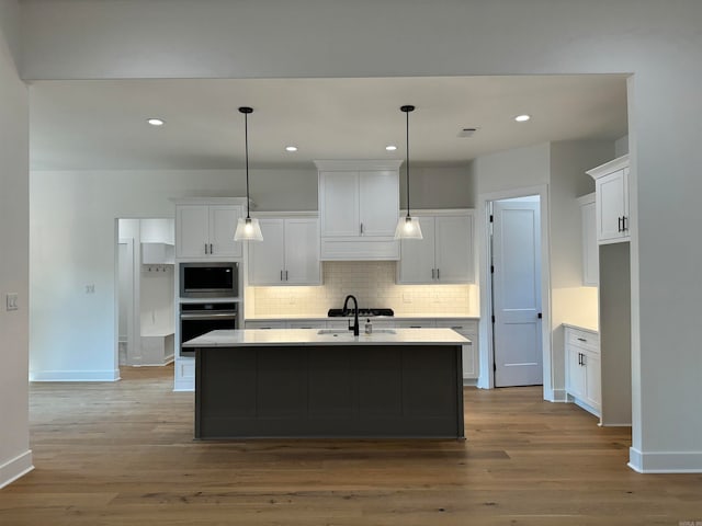 kitchen featuring wood-type flooring, white cabinets, a center island with sink, and appliances with stainless steel finishes