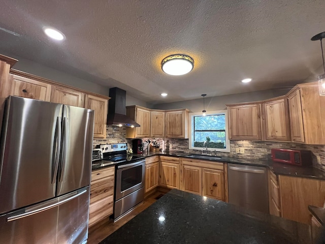 kitchen with pendant lighting, stainless steel appliances, backsplash, and wall chimney range hood