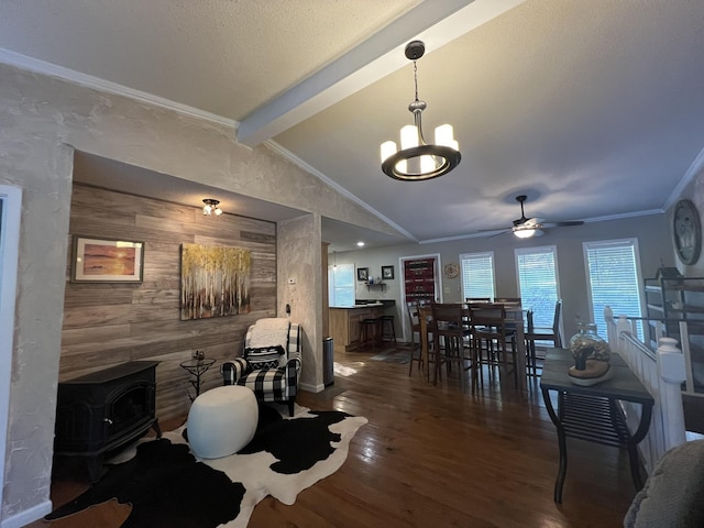 dining room featuring a wood stove, wood finished floors, wooden walls, vaulted ceiling with beams, and ceiling fan with notable chandelier