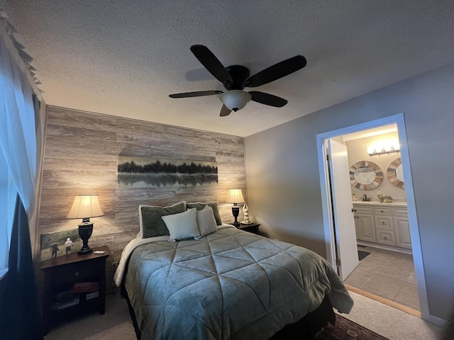 bedroom featuring ceiling fan, light colored carpet, ensuite bath, a textured ceiling, and an accent wall
