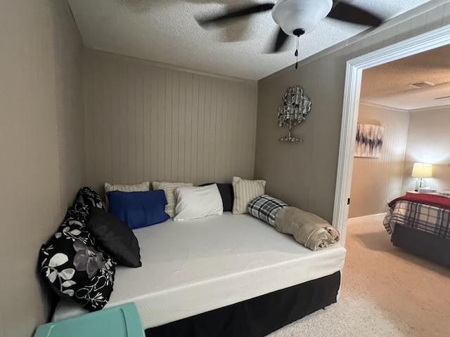bedroom featuring ceiling fan, a textured ceiling, visible vents, wooden walls, and carpet