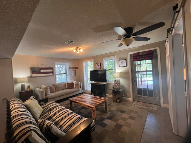 tiled living room featuring wood walls, ceiling fan, and a textured ceiling