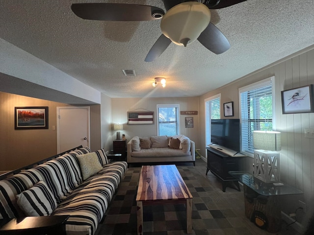 living room with ceiling fan, a textured ceiling, and wooden walls