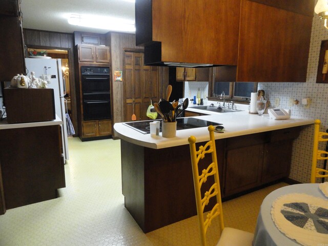 kitchen with sink, kitchen peninsula, a kitchen bar, white fridge, and black double oven