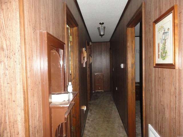 hall featuring wooden walls, dark colored carpet, and a textured ceiling