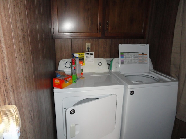 clothes washing area with cabinets, wooden walls, and independent washer and dryer