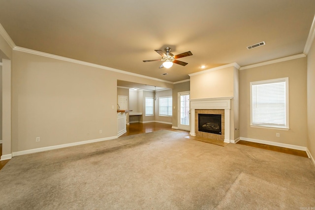 unfurnished living room featuring ceiling fan, carpet floors, crown molding, and a tile fireplace