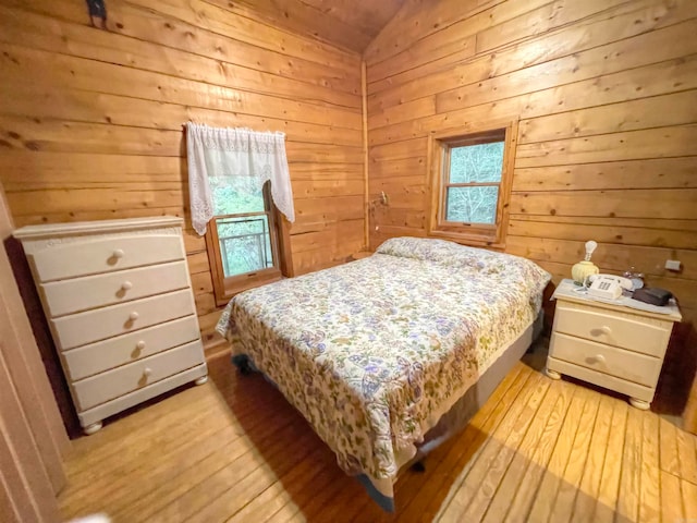 bedroom with light hardwood / wood-style flooring, wood walls, and lofted ceiling