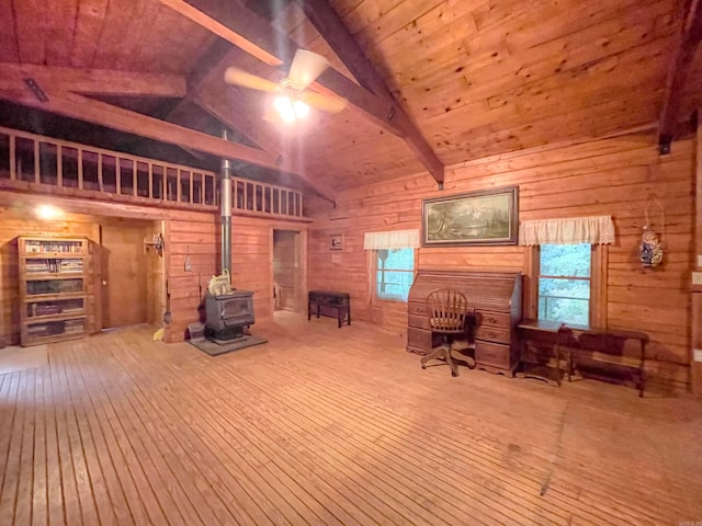 interior space with lofted ceiling with beams, a wood stove, ceiling fan, and a wealth of natural light