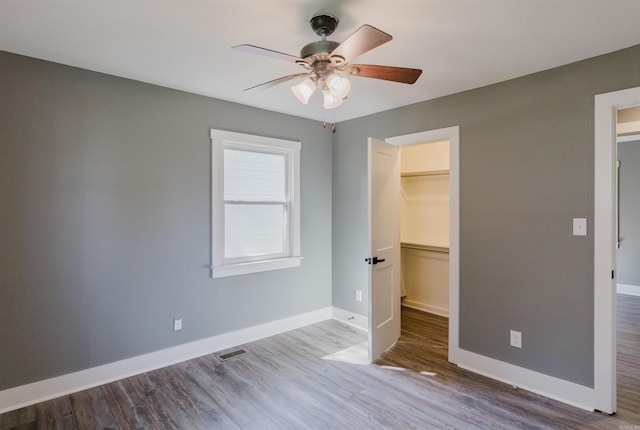 unfurnished bedroom featuring ceiling fan, a closet, wood-type flooring, and a walk in closet