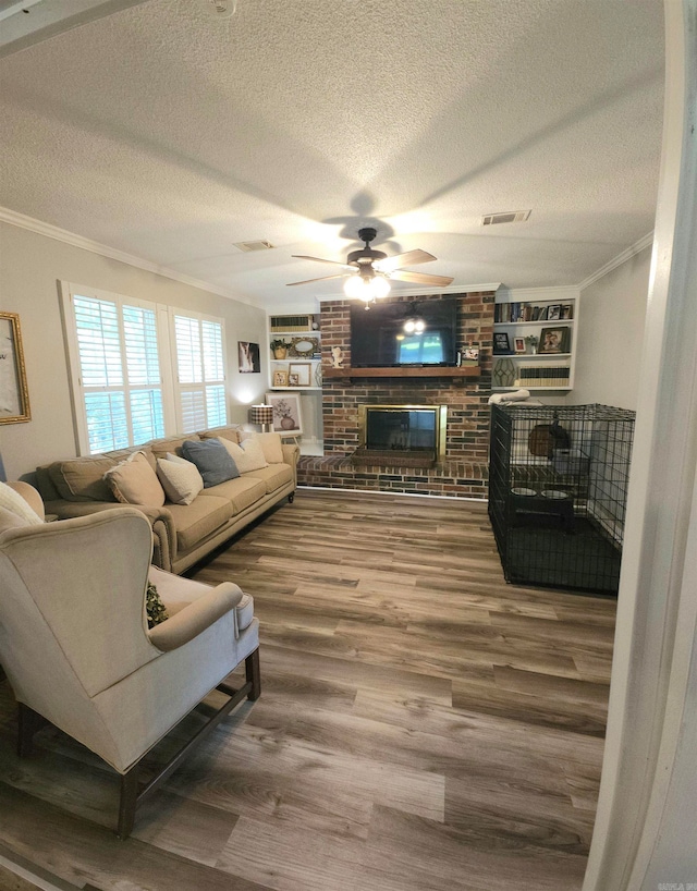 living room featuring ceiling fan, a textured ceiling, a fireplace, crown molding, and hardwood / wood-style floors