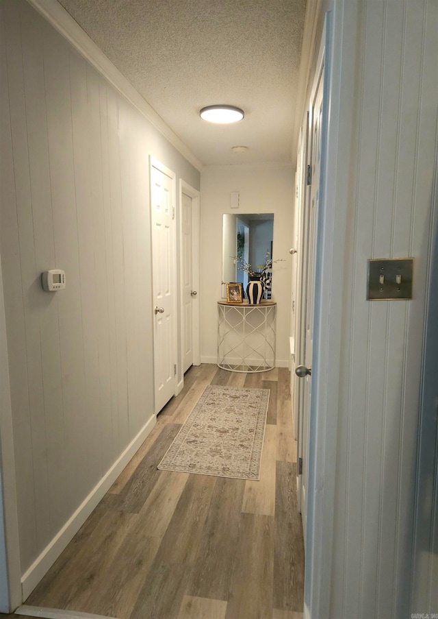 corridor featuring a textured ceiling, ornamental molding, and hardwood / wood-style flooring