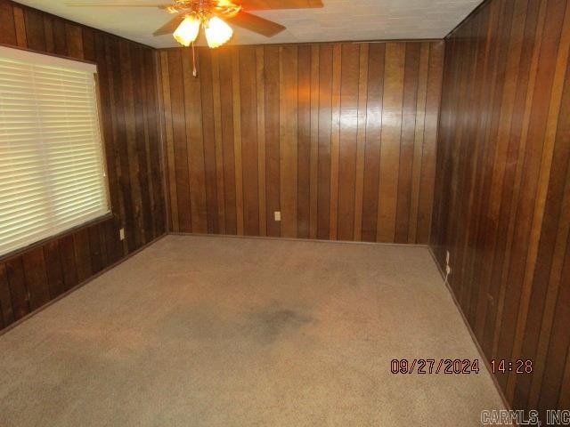 unfurnished room with carpet flooring, wood walls, and ceiling fan