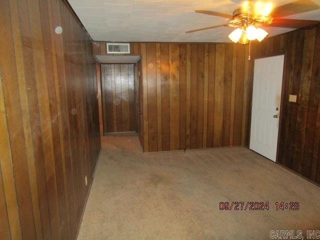 spare room with light carpet, wooden walls, and ceiling fan