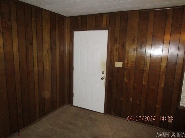 entrance foyer with wood walls and dark colored carpet