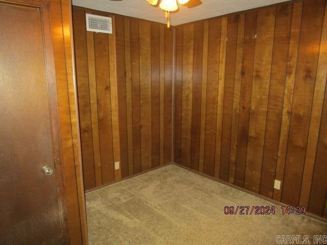 carpeted spare room featuring wood walls and ceiling fan