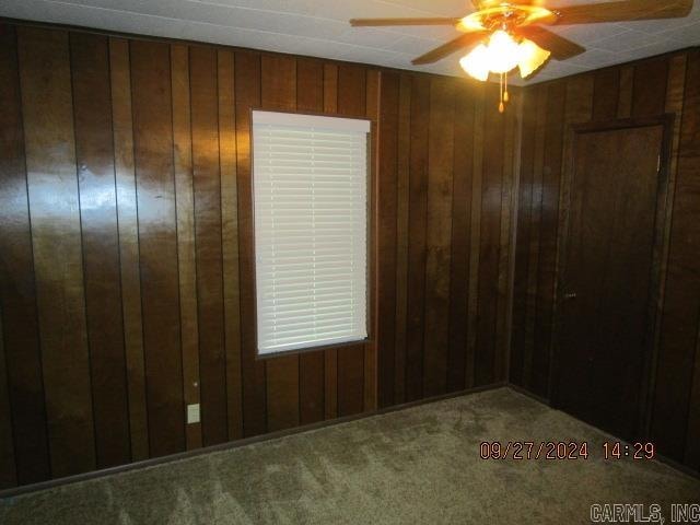 carpeted empty room featuring ceiling fan and wooden walls